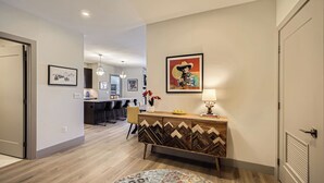 A modern living room with a wooden floor, a dining area with a round rug, and a kitchen in the background. - Blue River Parkway’s Colorful Escape (Silverthorne)