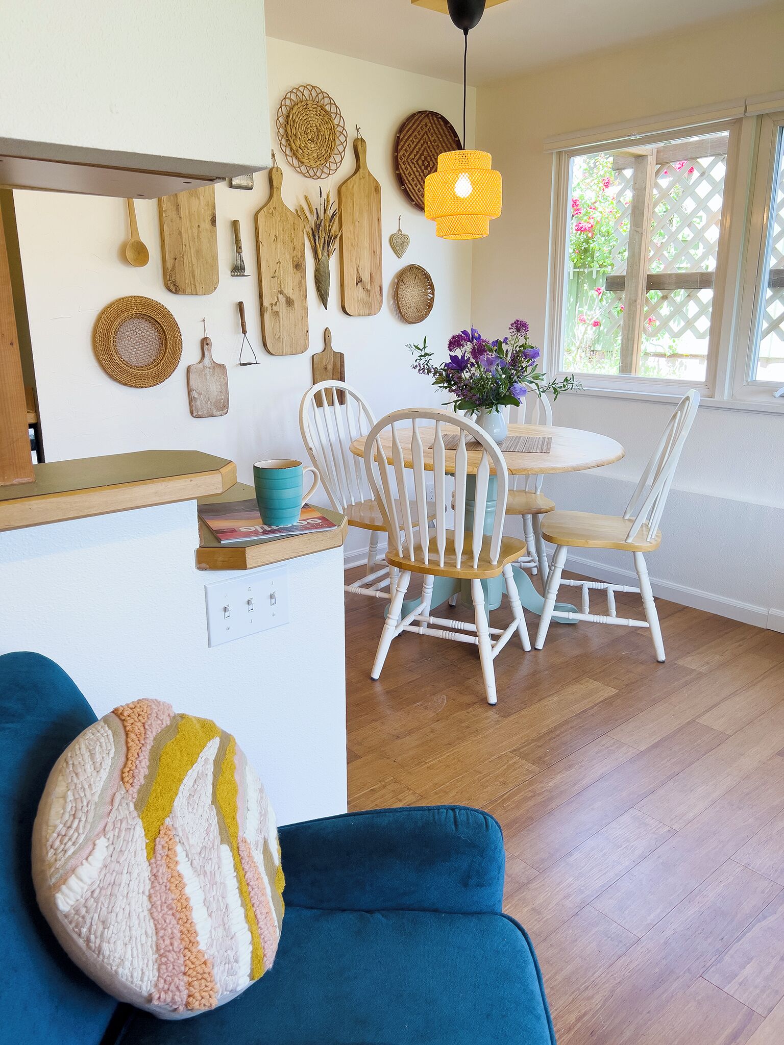 A cozy dining area with a round wooden table, white chairs, and a vase of flowers.