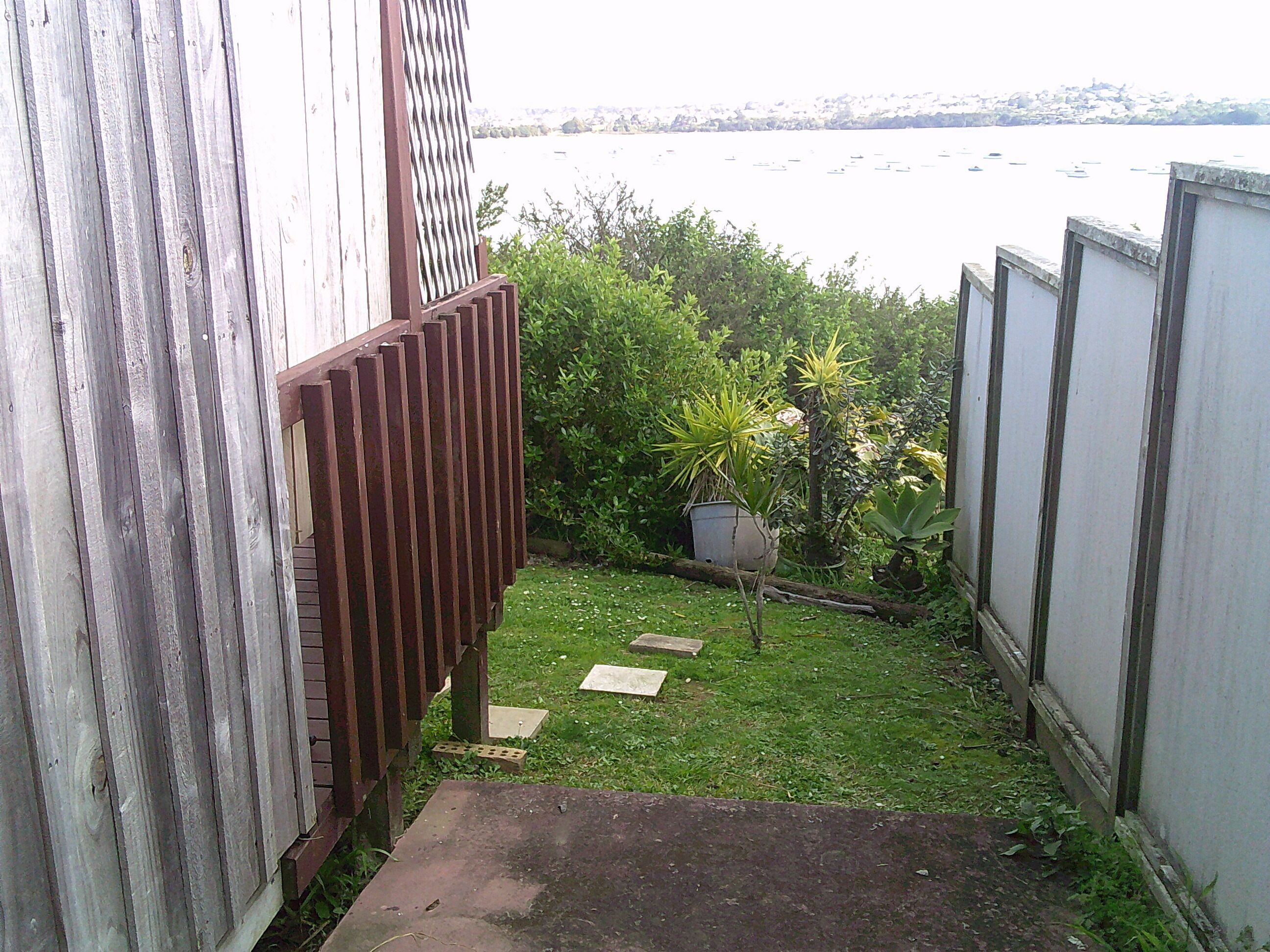 A narrow pathway leading to a grassy area with a view of a body of water and a distant shoreline.