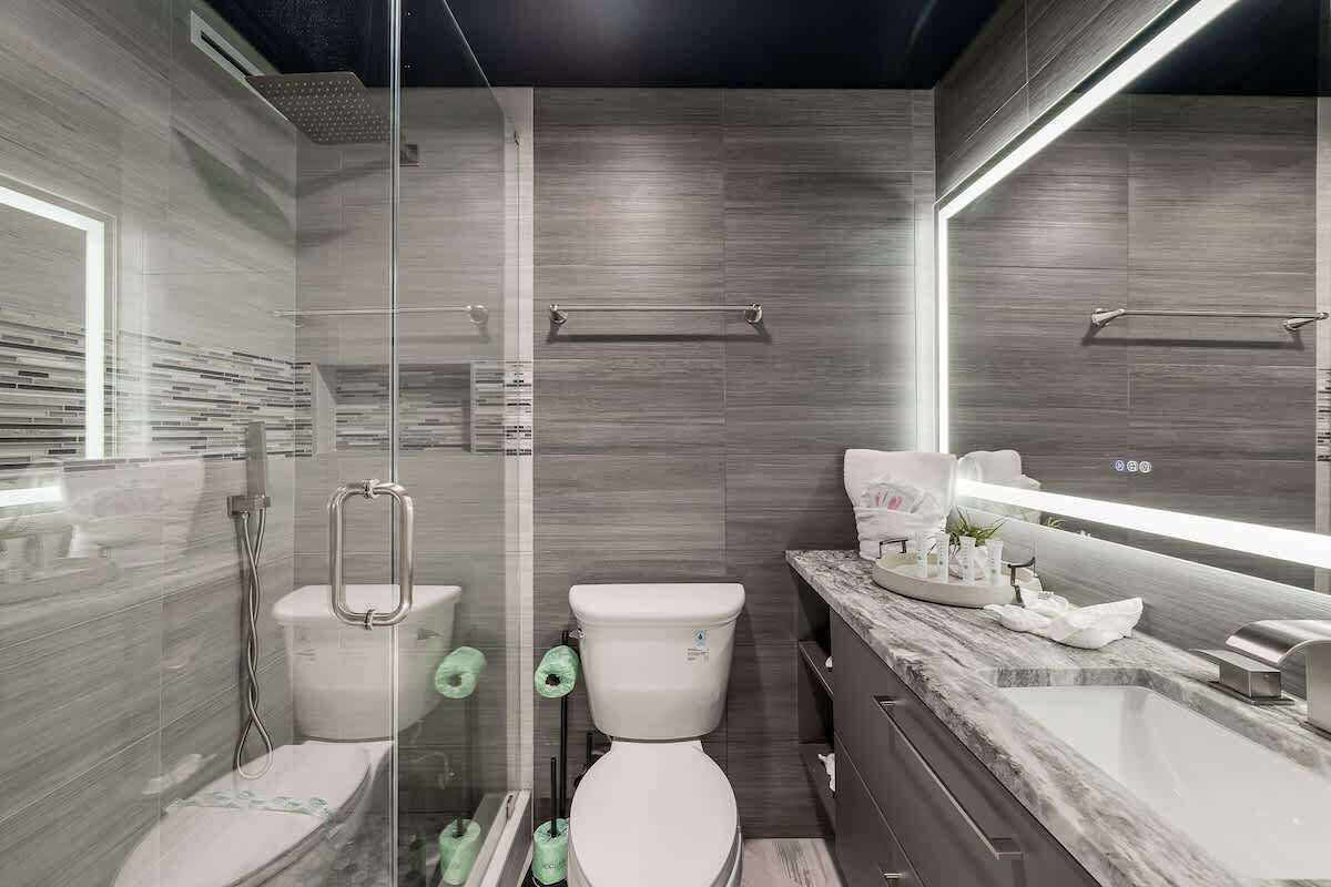 Un baño moderno con cabina de ducha de vidrio, dos inodoros, encimera de mármol y un espejo grande.