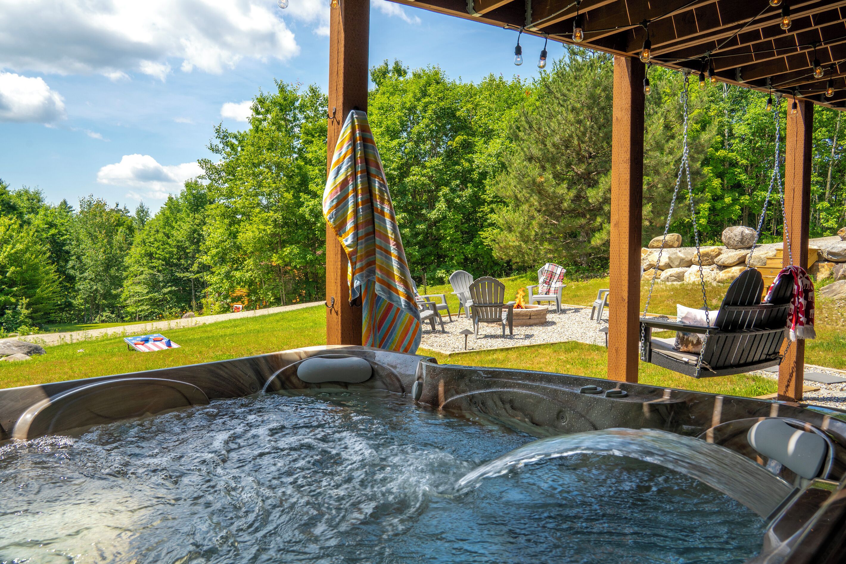 Un jacuzzi con una pérgola de madera encima, rodeado de asientos exteriores y vistas a árboles.