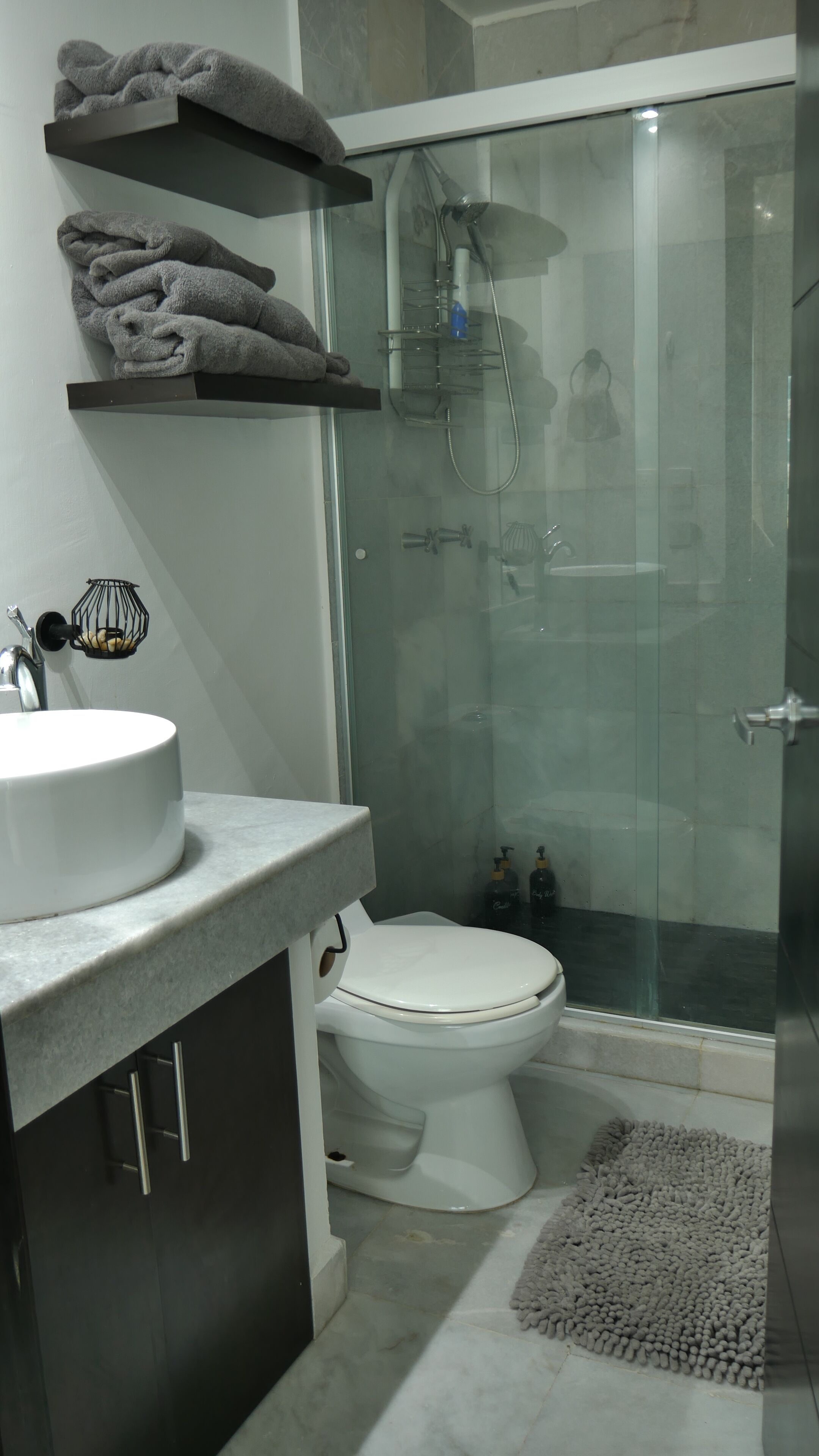 Et moderne badeværelse med et glasafskærmet brusebad, et hvidt toilet og en marmorvask.