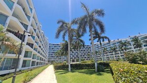 A modern hotel with multiple floors, a central pathway, and palm trees. - Aria Ocean Nuevo Vallarta Beach Pool (Nuevo Nayarit)