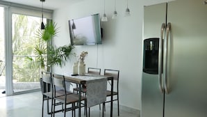 A modern kitchen with a dining table, chairs, a refrigerator, a TV, and hanging pendant lights. - Aria Ocean Nuevo Vallarta Beach Pool (Nuevo Nayarit)