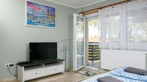 A bedroom with a bed, a TV, a painting, and a window with curtains.