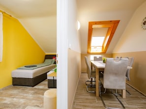 A small, bright room with a bed, a dining table with chairs, and a skylight.