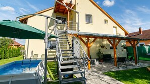 A two-story house with a swimming pool, a covered patio, and a wooden staircase leading to the upper floor.