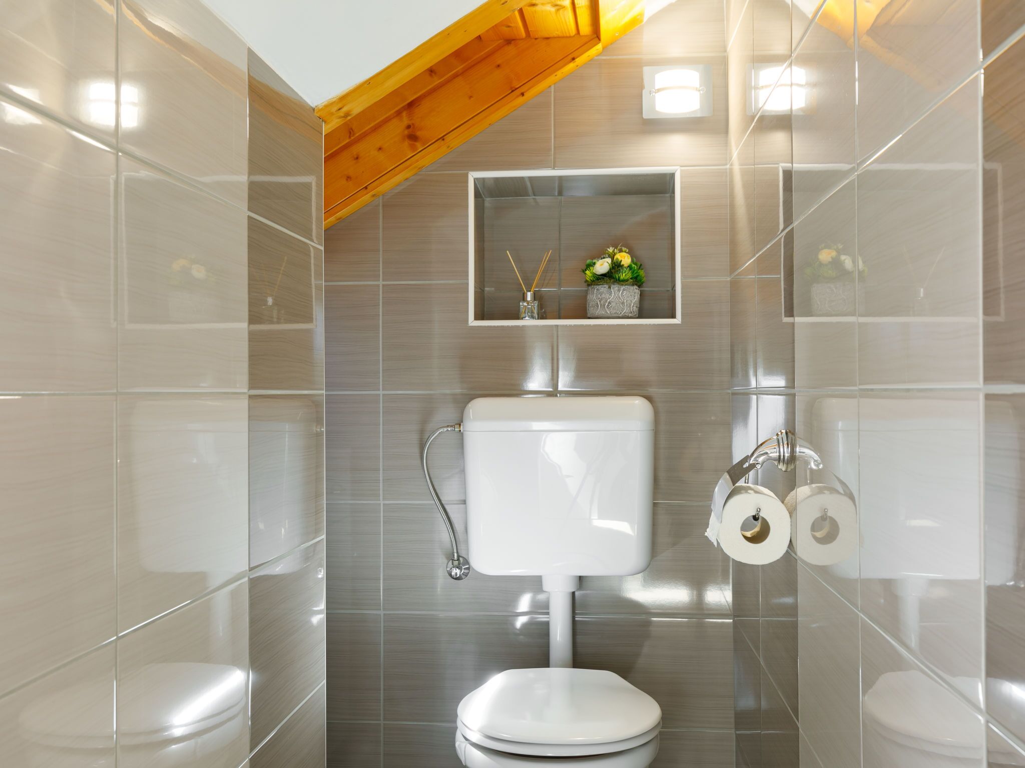 Un baño moderno con un inodoro blanco, una repisa con artículos de aseo y una viga de techo de madera.