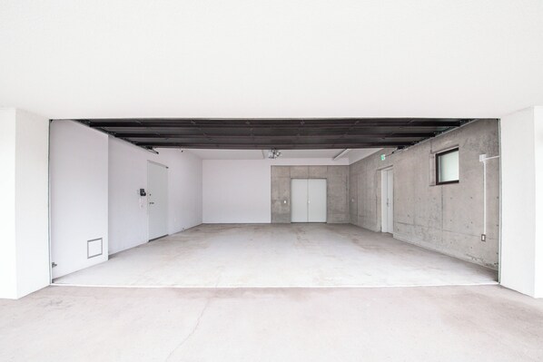 A spacious, empty room with a concrete floor, white walls, and a dark ceiling beam.