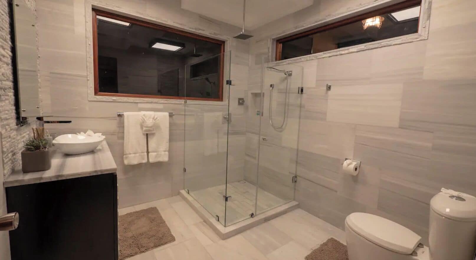 A modern bathroom with a glass-enclosed shower, a sink with a vase, and a toilet.