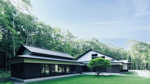 Une maison moderne à deux étages, dotée d’une grande pelouse à l’avant et d’un arbre planté devant.