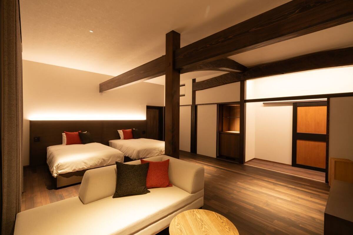 Une chambre d’hôtel avec deux lits, un canapé, un plancher en bois et une grande fenêtre.