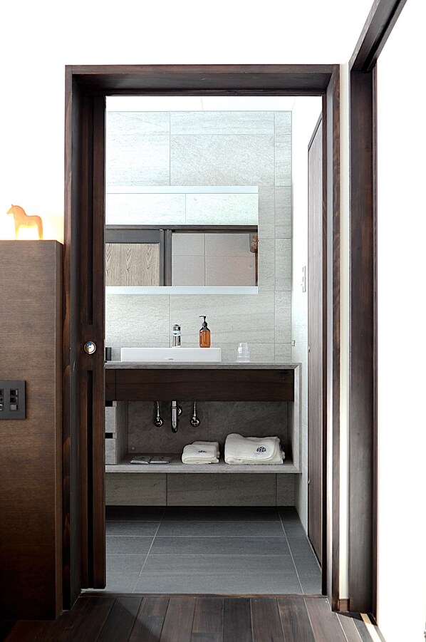 Un baño moderno con una puerta de madera oscura, un lavamanos blanco, un espejo y un perchero para toallas.