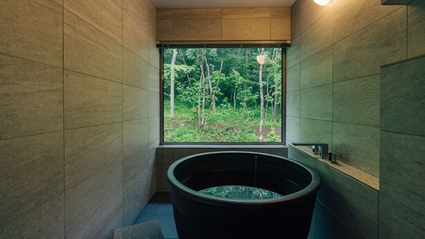 Une salle de bain moderne dotée d’une grande baignoire, d’une fenêtre donnant sur la forêt et d’une étagère intégrée pour les articles de toilette.