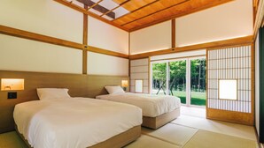 Une pièce de style japonais traditionnel, dotée de deux lits, d’un sol recouvert de tatamis, de portes coulissantes et offrant une vue sur la verdure environnante.