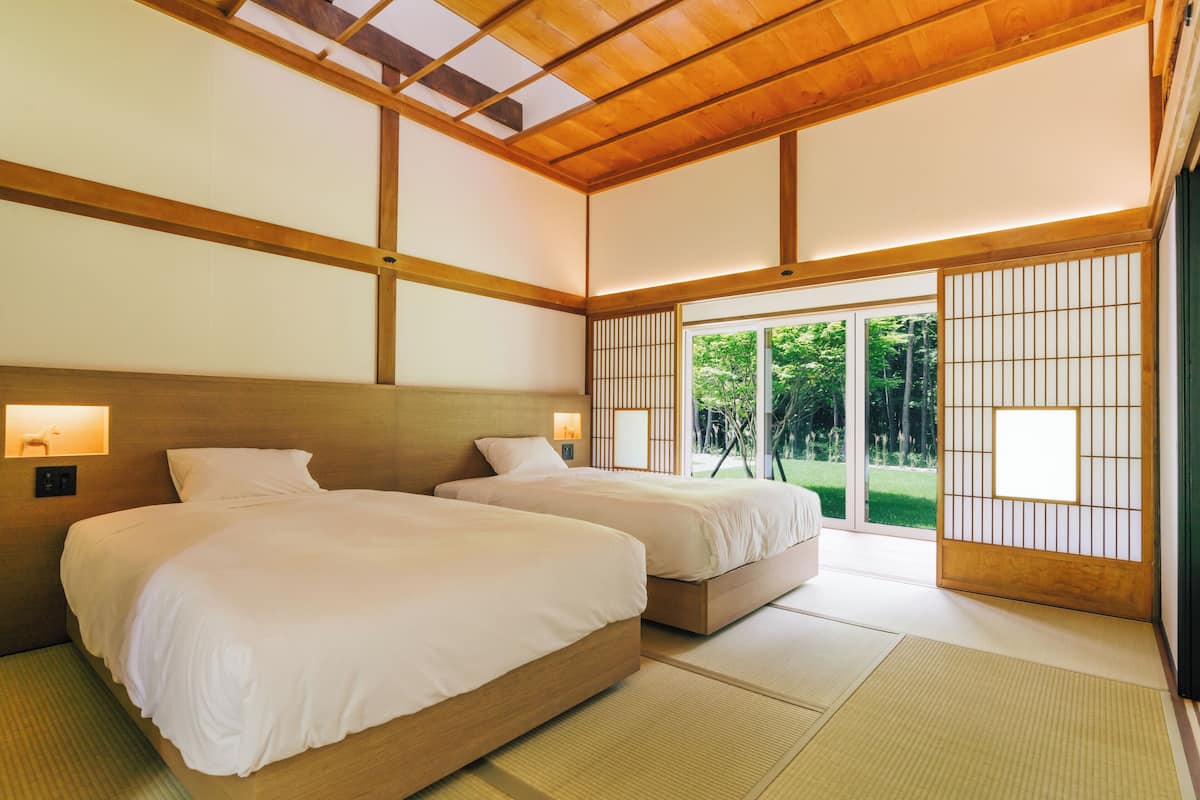 Une pièce de style japonais traditionnel, dotée de deux lits, d’un sol recouvert de tatamis, de portes coulissantes et offrant une vue sur la verdure environnante.
