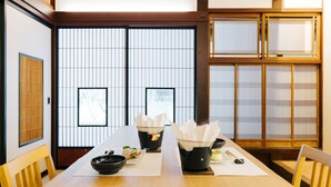 Une pièce de style japonais traditionnel, avec un sol recouvert de tatamis, des portes coulissantes et une petite table sur laquelle se trouvent un bol noir et des baguettes.