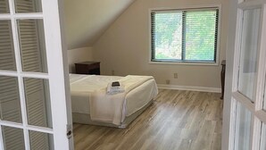 A bedroom with a sloped ceiling, a bed, a nightstand, a window with blinds, and a door with a glass panel. - Cozy Amazing Suite  (Willmar)