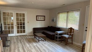 A living room with a sofa, a wooden coffee table, a chair, a desk, and a window with blinds. - Cozy Amazing Suite  (Willmar)