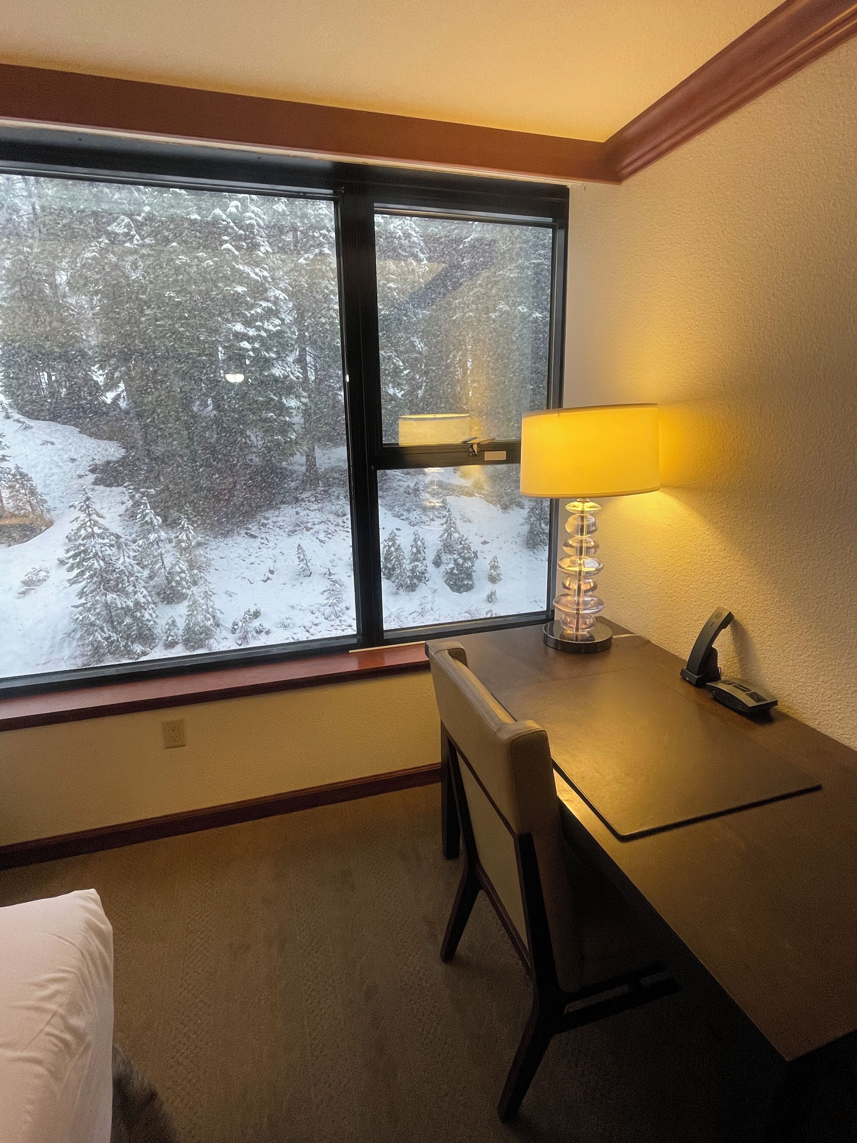 A hotel room with a large window, a table with a lamp, and a chair.