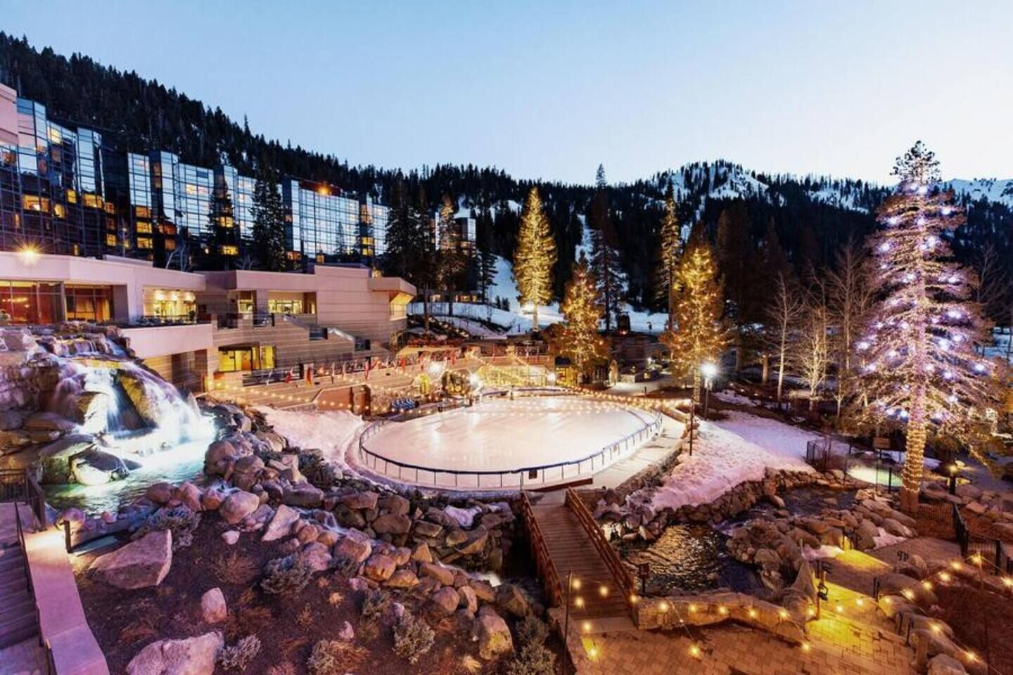Un hôtel doté d’une grande patinoire en plein air, entouré d’arbres couverts de neige et avec une chaîne de montagnes en toile de fond.