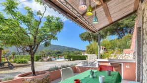 En udendørs terrasse med et bord dækket til to, omgivet af stenplantere og udsigt til et bjergrigt landskab.