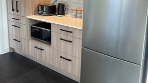 Una cocina moderna con armarios de madera clara, un refrigerador de acero inoxidable, horno empotrado y encimera con hervidor y tostadora.