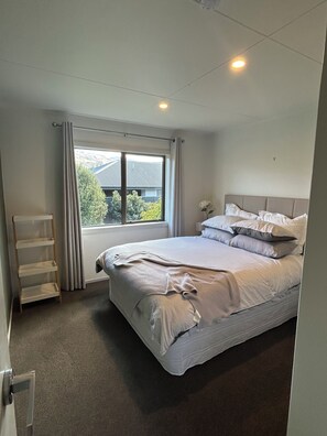 A bedroom with a bed, a window, a radiator, and a shelf. - Elevated Mountain Views on Waenga (Cromwell)