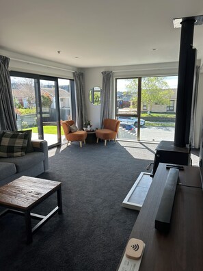 A modern living room with a sofa, two armchairs, a coffee table, and a flat-screen TV. - Elevated Mountain Views on Waenga (Cromwell)