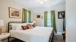 Un dormitorio ordenado con cama, mesita de noche, lámpara y ventilador de techo.