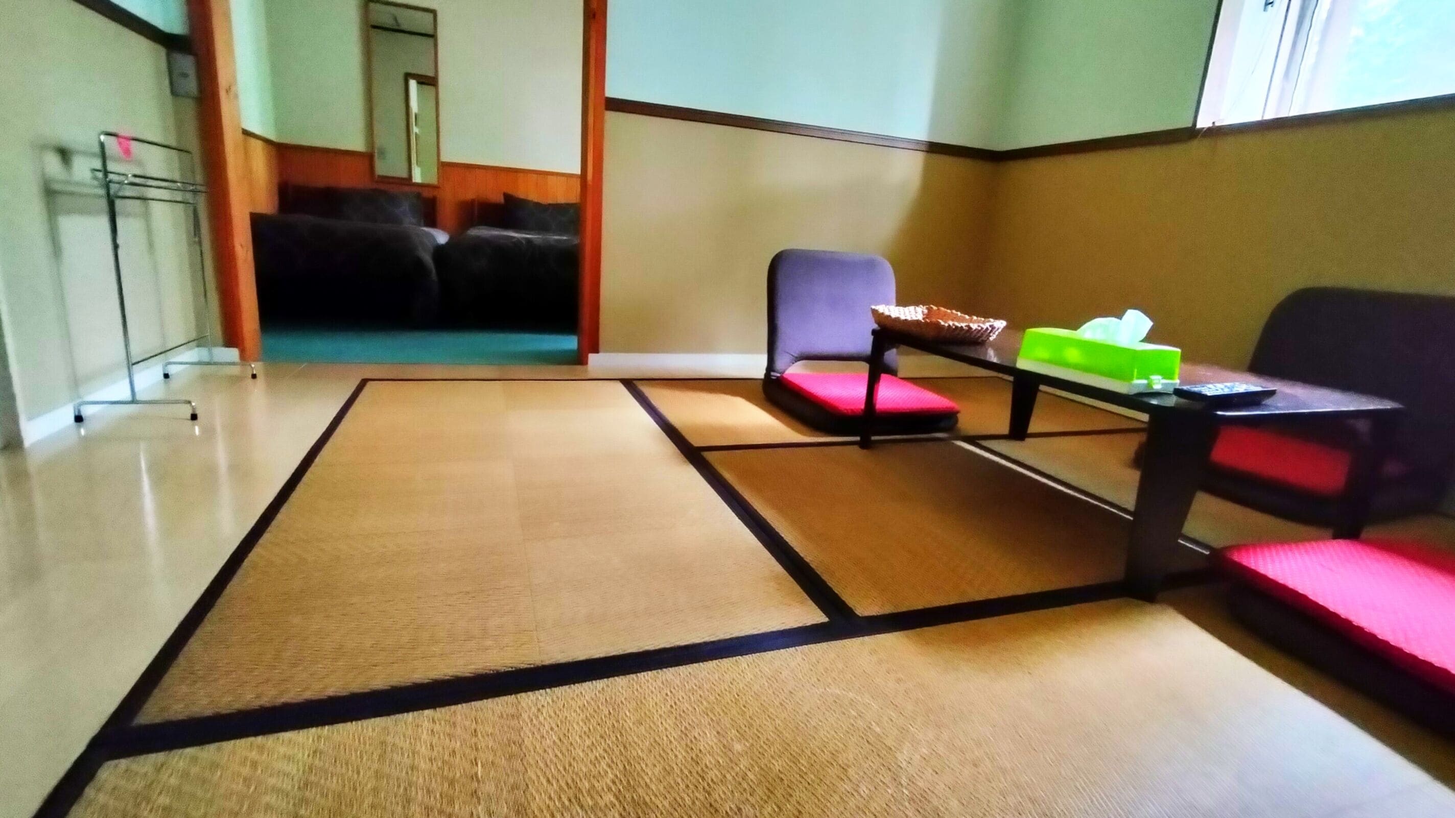 A tatami mat room with a sofa, a small table with a green box, and a chair.