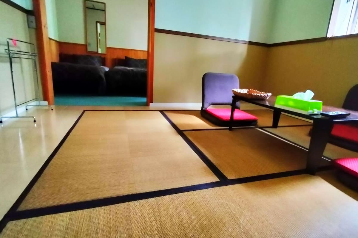 A room with tatami mats, a small table with a green box, and a chair with a red cushion.