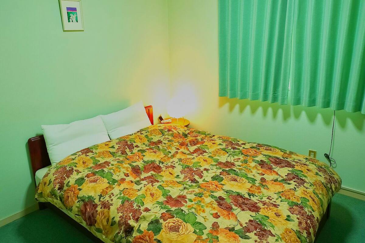 A room with a bed, a bedside table, a lamp, a framed picture on the wall, and a window with curtains.