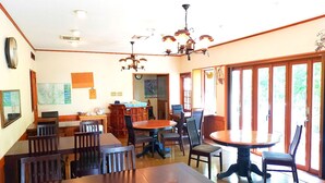 Un comedor con mesas y sillas de madera, una araña y vistas amplias a través de grandes ventanales.