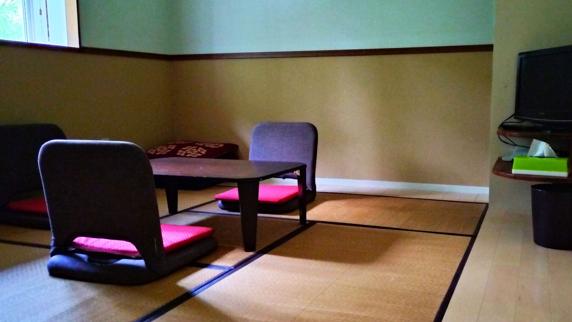 A room with tatami flooring, a low table, and two chairs with cushions.