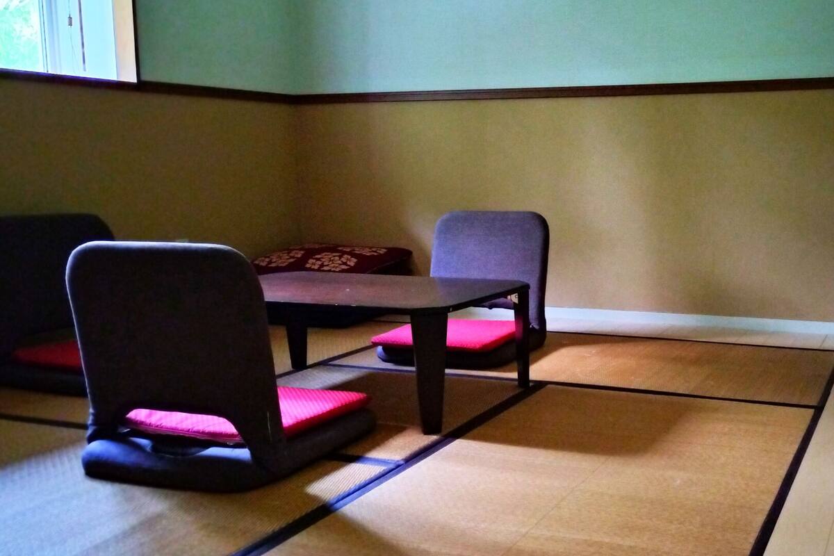 A room with tatami flooring, a low table, and two chairs with cushions.
