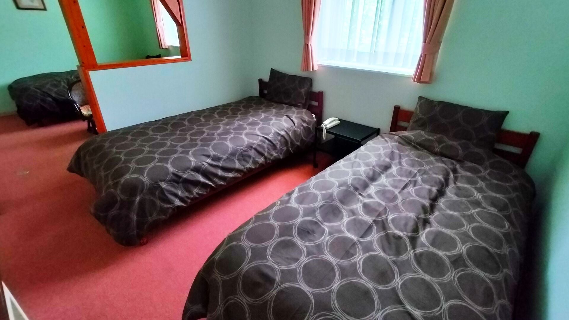 A room with two single beds, a small table, a telephone, and a mirror.