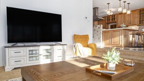Una sala de estar con un televisor de pantalla plana grande, una mesa de centro de madera y un sillón amarillo.