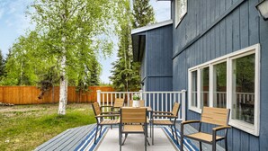 Una terraza con una mesa y sillas, una valla de madera y un edificio azul con detalles blancos.
