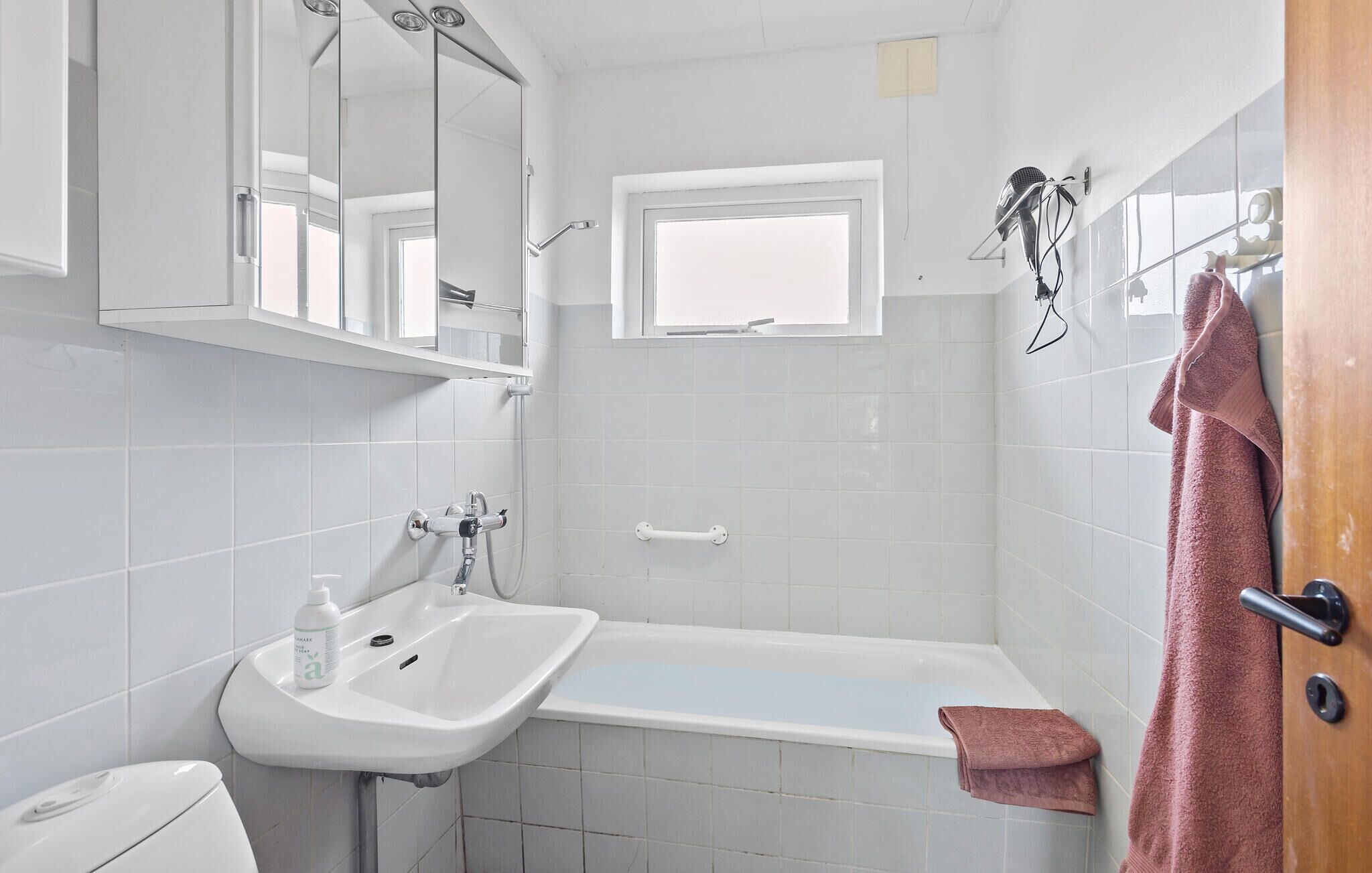 Un baño con lavamanos blanco, bañera, espejo y ventana.