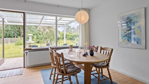 Un coin repas avec une table ronde en bois, six chaises et une grande fenêtre donnant sur un jardin.