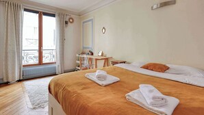 Ein Hotelzimmer mit Bett, zwei Handtüchern, Schreibtisch, Stuhl, einem Fenster mit Vorhängen und Blick auf den Außenbalkon.