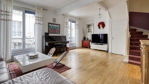 Ein geräumiges Wohnzimmer mit einem Klavier, einem Flachbildfernseher und einer Treppe, die zu einer oberen Etage führt.