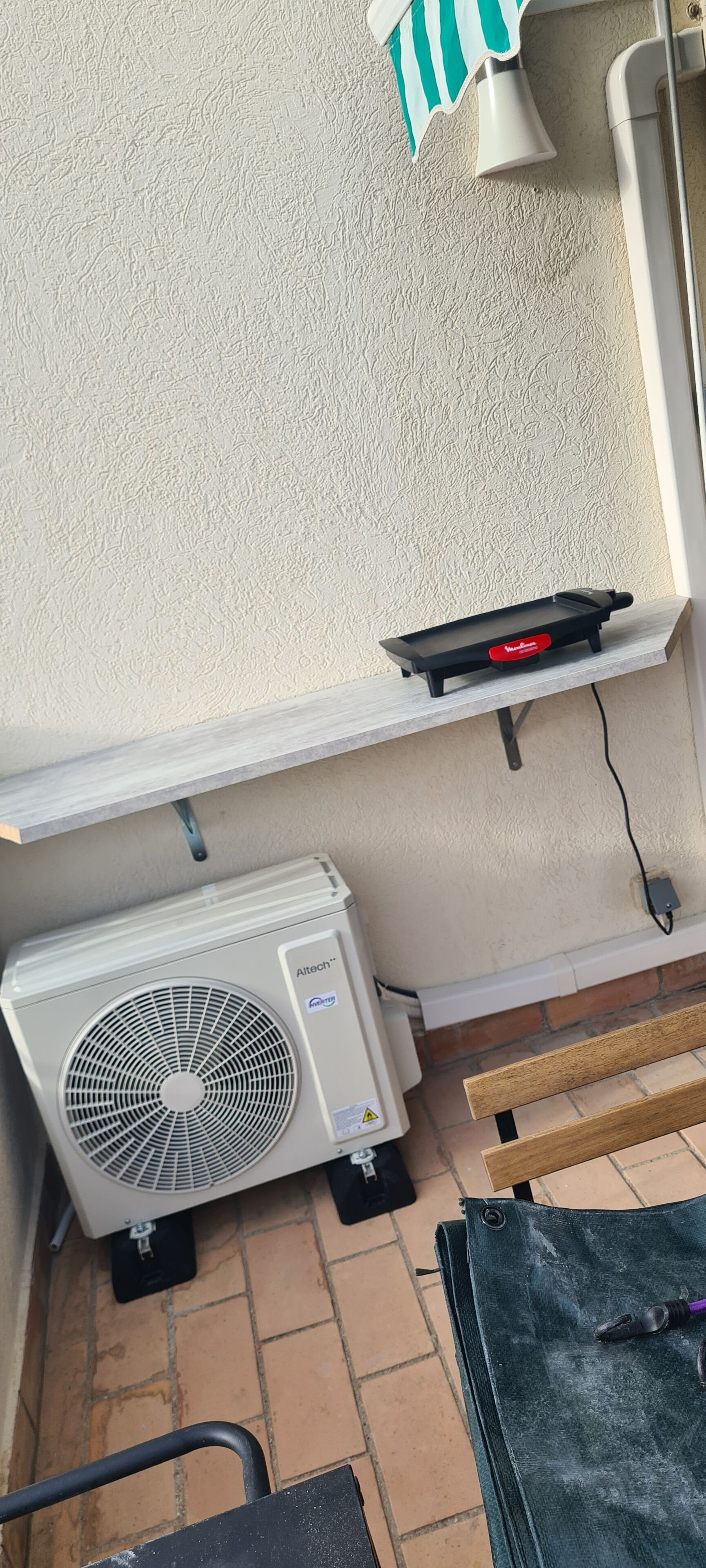 Eine Klimaanlage, ein Mehrfachsteckdosenadapter und eine Bank vor einer strukturierten Wand.