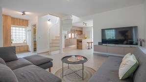 A modern living room with a sofa, a coffee table, and a TV. There is a kitchen area with a staircase leading to another level. - Lovely home in Vrgorac with WiFi (Vrgorac)