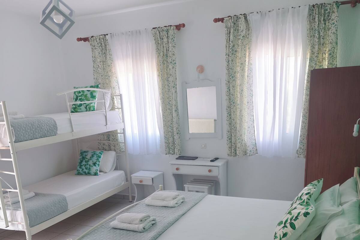 A well-lit room with bunk beds, a small desk, a mirror, and a window with curtains.