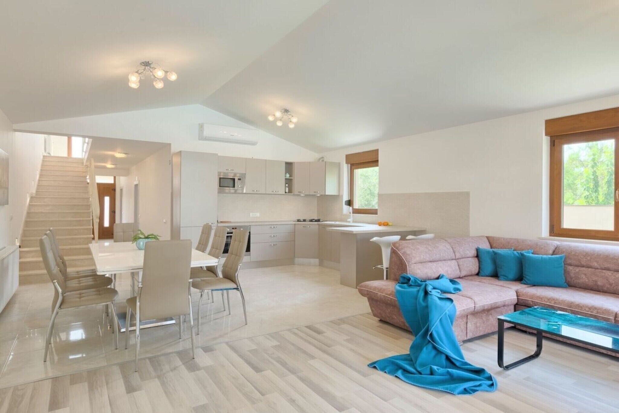 Un vaste espace de vie comprenant un canapé, une table à manger avec des chaises, un coin cuisine et un escalier menant à un niveau supérieur.