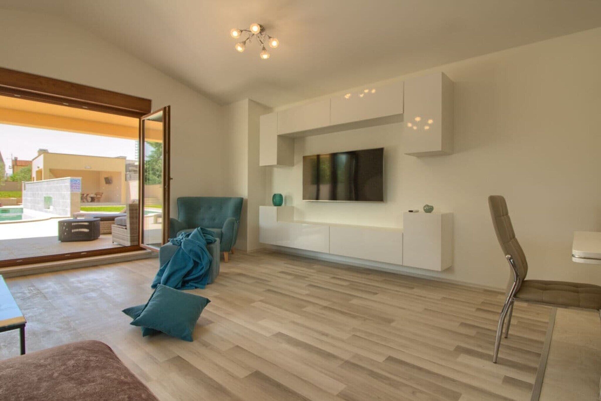 Een moderne woonkamer met een flatscreen televisie aan de muur, een bank, een fauteuil en een salontafel.