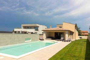 Una casa moderna con piscina, un patio con sillones de descanso y un césped bien cuidado.