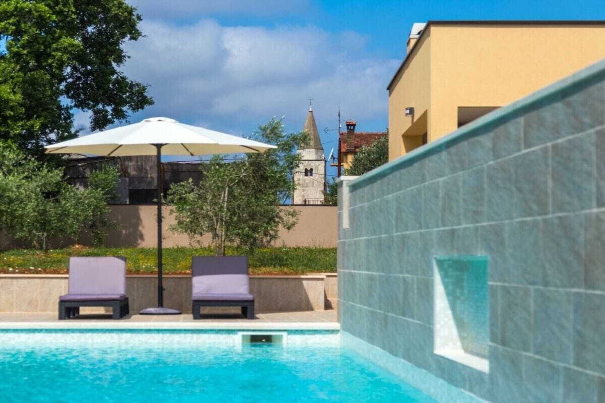 Ein Pool mit Liegestühlen und Sonnenschirm, im Hintergrund ein Stein-Turm und ein Gebäude mit einer Kachelfassade.